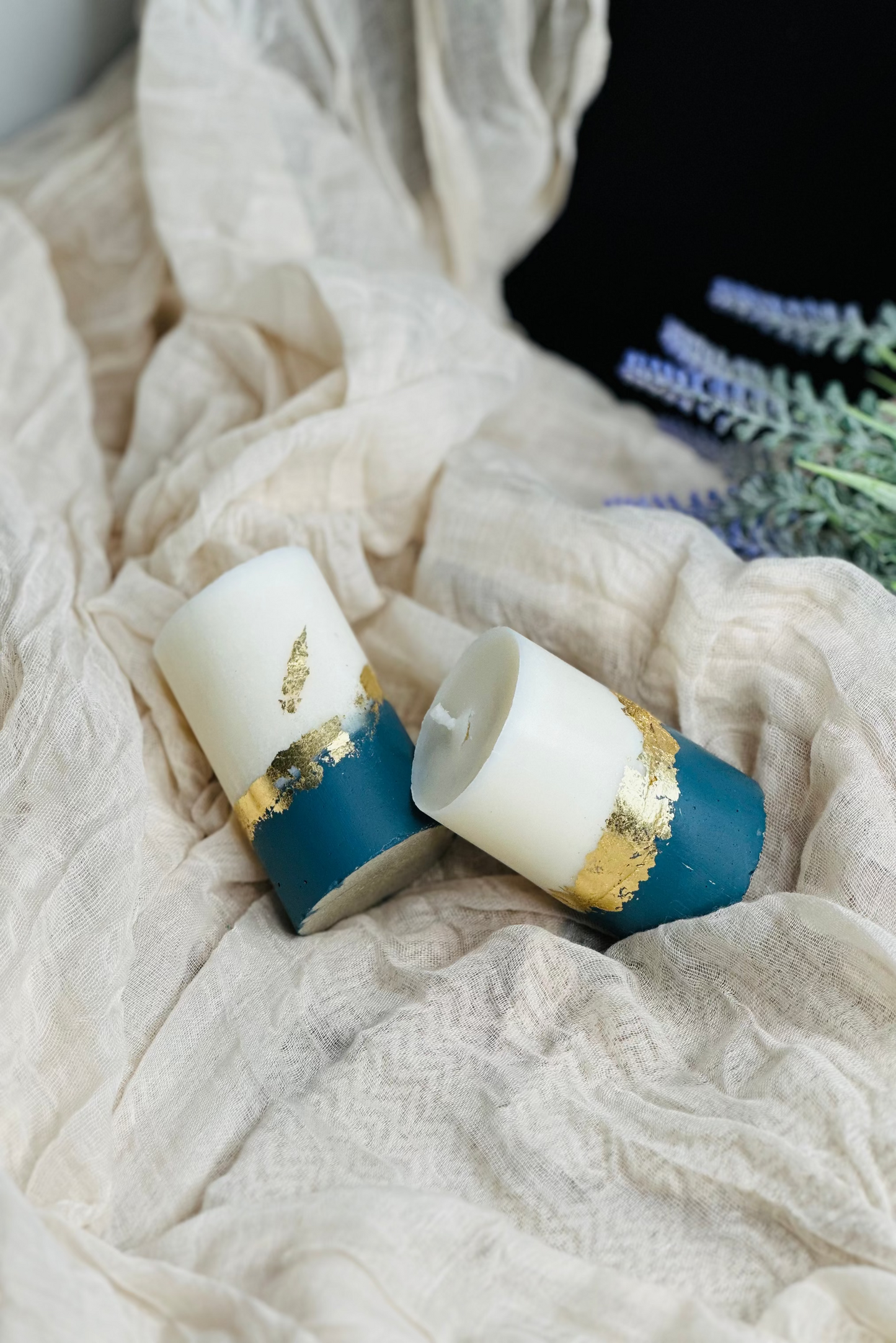 Two cylindrical candles with blue and gold accents on a textured fabric surface - UK made