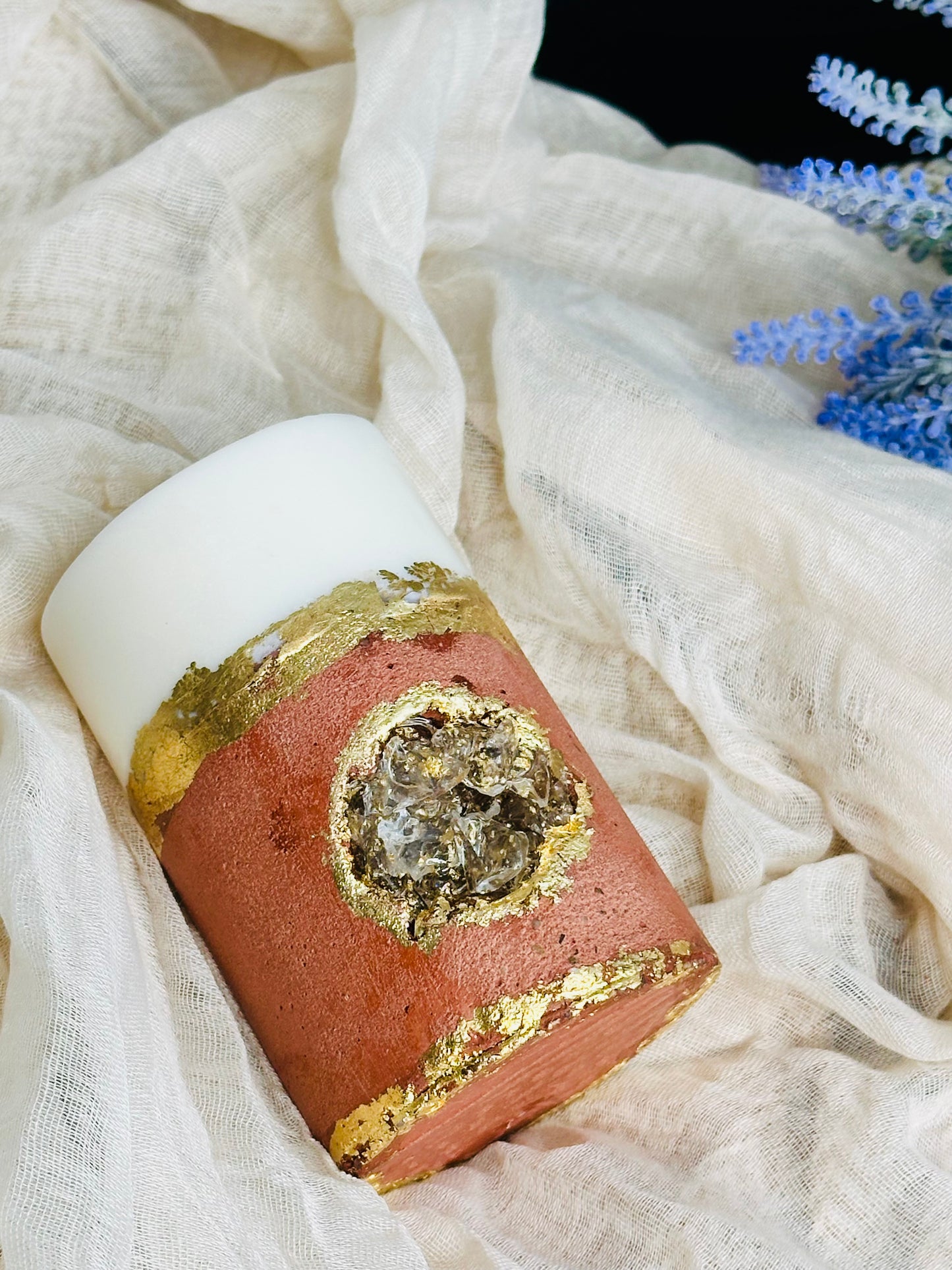 Decorative candle with gold and red design on a white fabric background