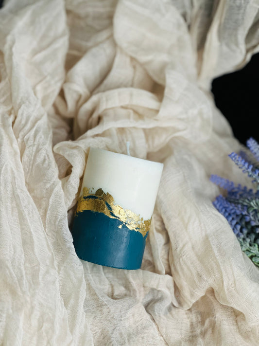 Candle with gold leaf design on a white fabric background