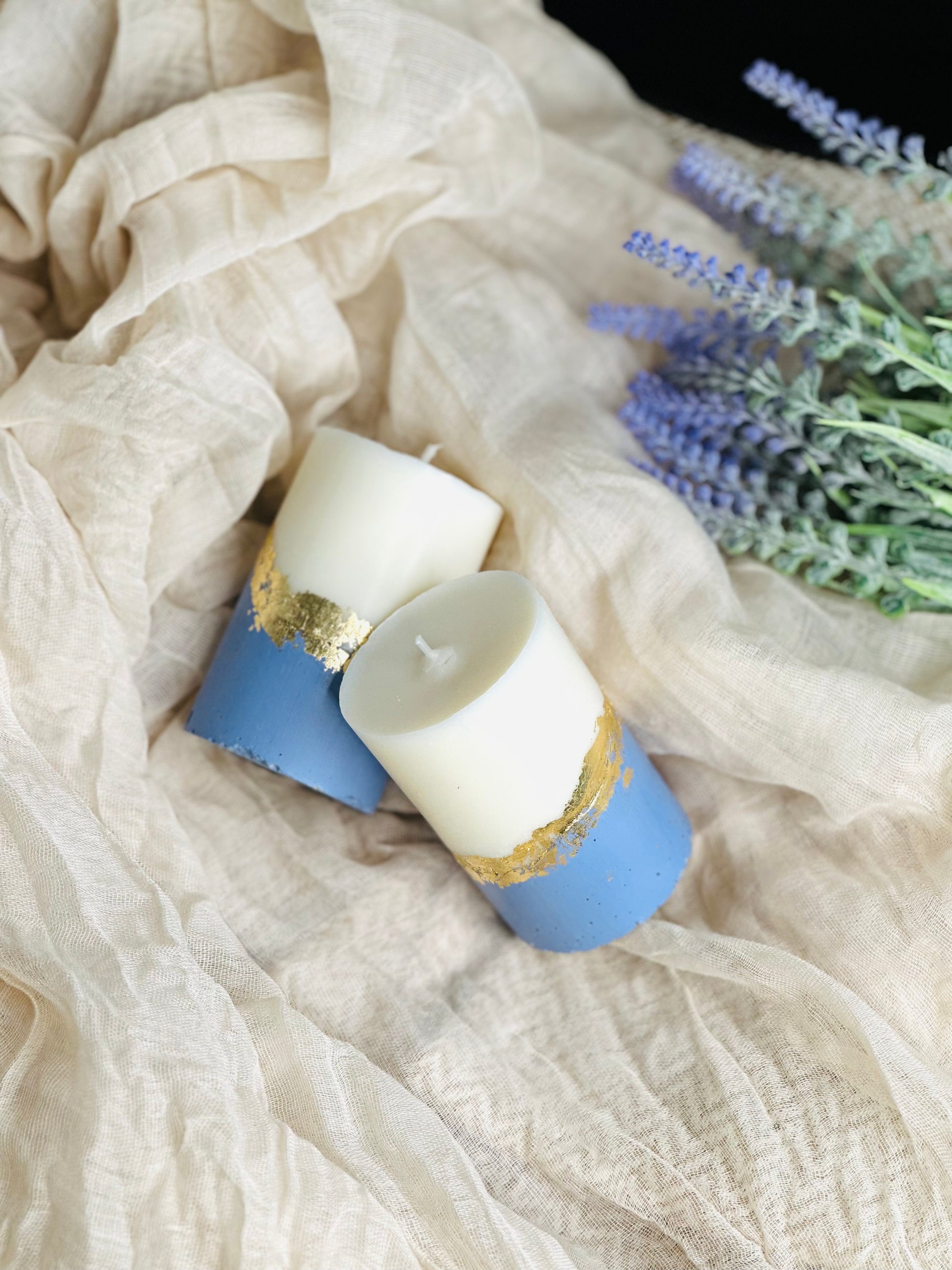 Two candles with gold accents on a blue base, surrounded by lavender and cheesecloth - UK made