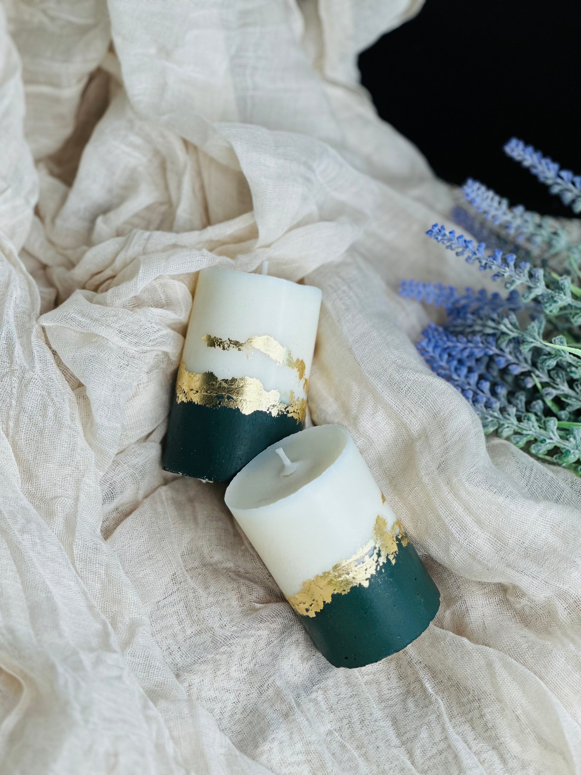 Two candles with gold accents on a textured fabric background with lavender flowers - UK made